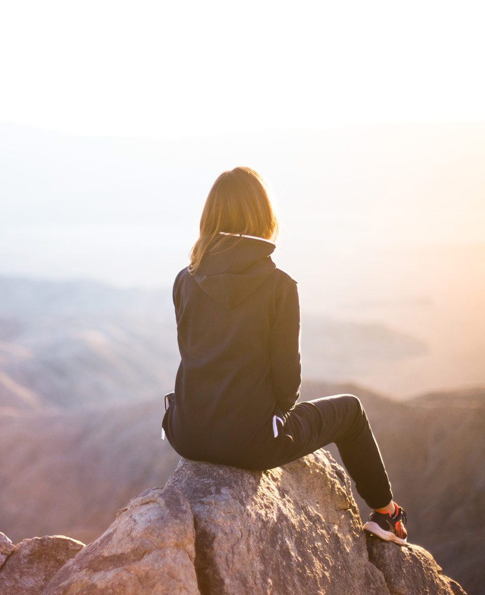 Chica sentada en una roca mirando al horizonte
